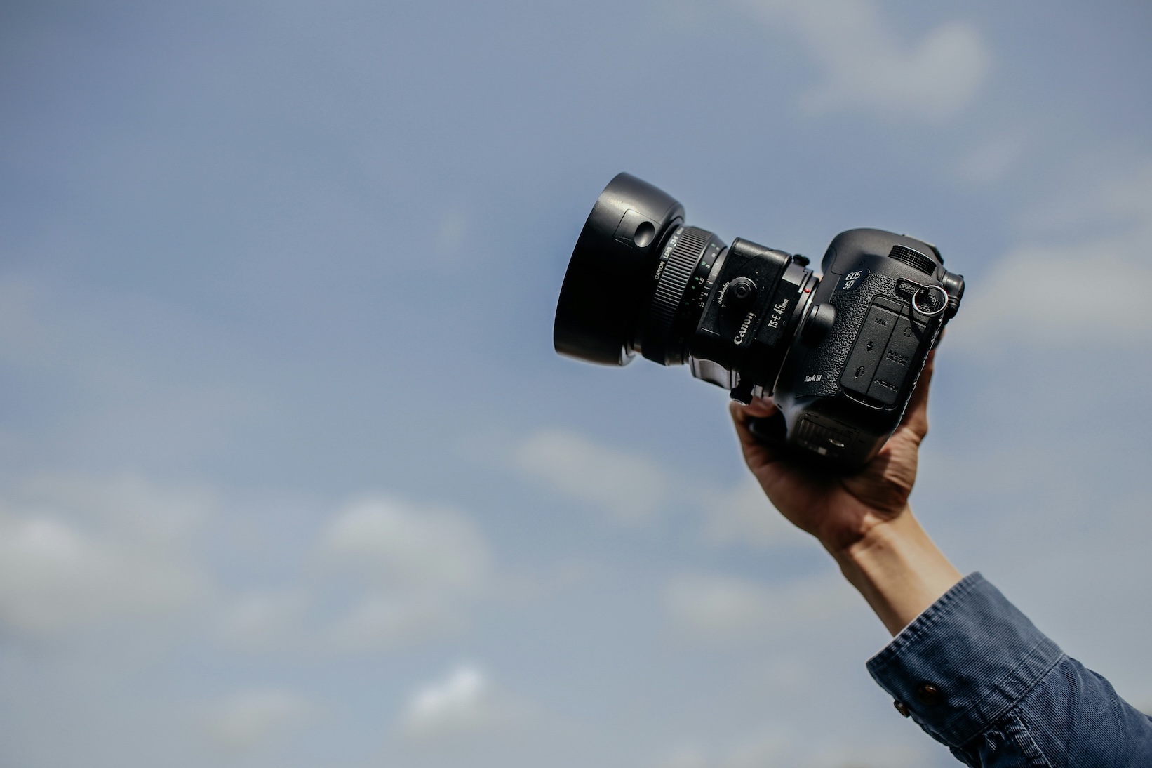 Hand holding a Canon camera against a blue sky